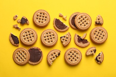 Tasty sandwich cookies with cream on yellow background, flat lay