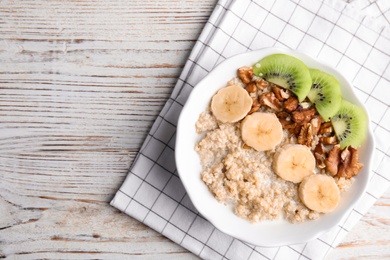 Photo of Bowl of quinoa porridge with walnuts, kiwi, banana and milk on wooden background, top view. Space for text