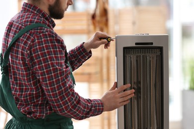 Professional technician repairing electric ultrared heater with screwdriver indoors, closeup