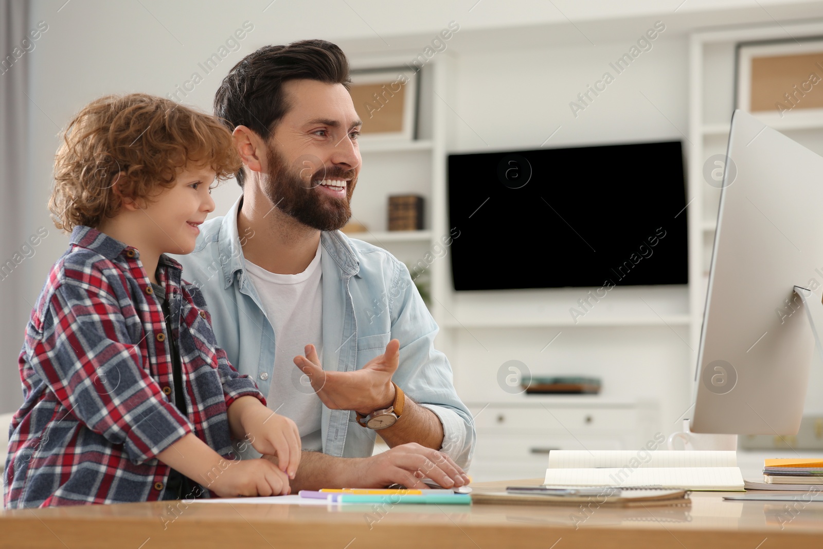 Photo of Remote work. Happy father introducing his son to colleagues via video chat at home. Man and child at desk