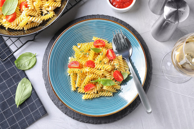 Delicious pasta with tomatoes and basil served on light table, flat lay