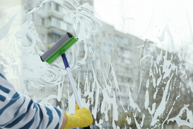 Photo of Woman cleaning window with squeegee at home, closeup. Space for text