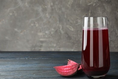 Photo of Cut beet and glass of juice on blue wooden table against grey background. Space for text