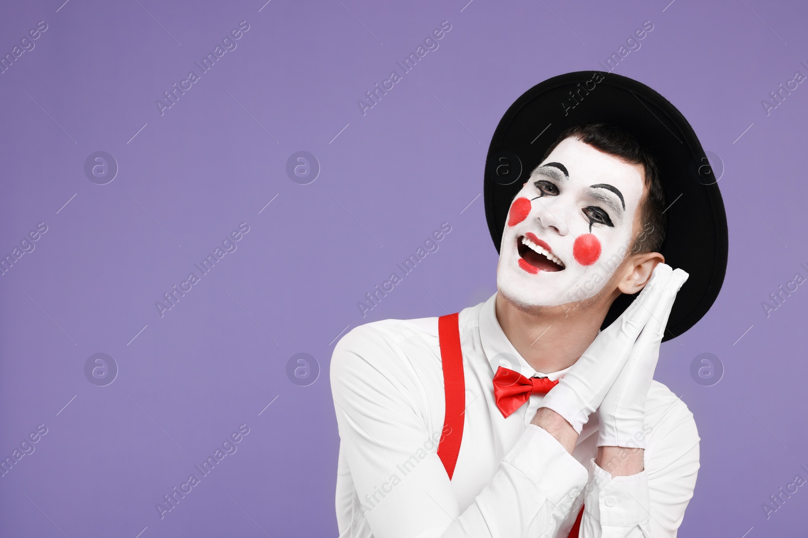 Photo of Funny mime artist posing on purple background. Space for text