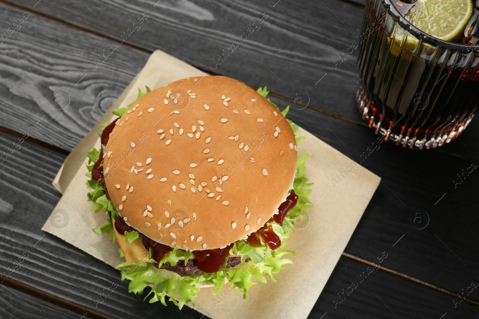 Photo of Burger with delicious patty and soda drink on black wooden table