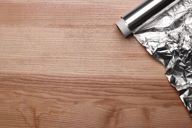 Photo of Roll of aluminum foil on wooden table, top view. Space for text