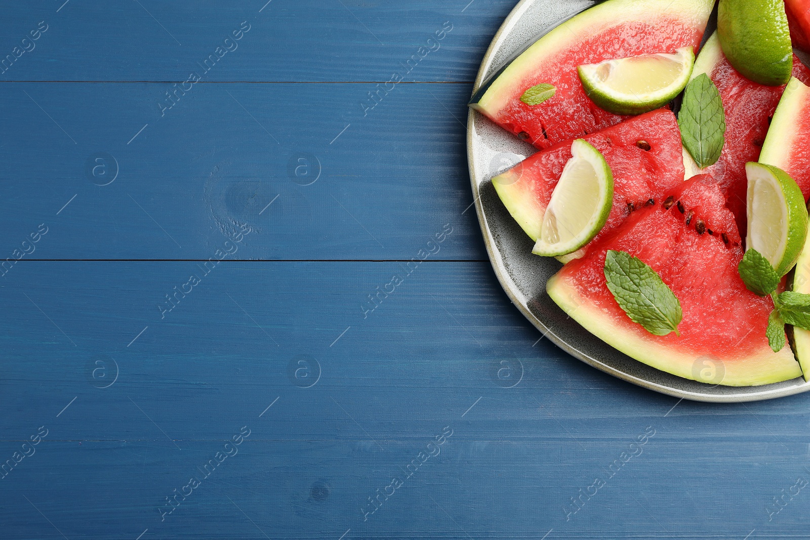 Photo of Plate with juicy watermelon and lime on blue wooden table, top view. Space for text