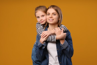 Photo of Little daughter hugging her mom on orange background. Happy Mother's Day