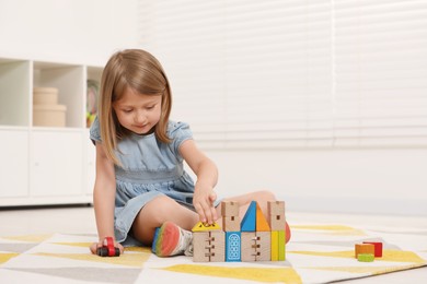 Photo of Cute little girl playing with wooden toys indoors, space for text