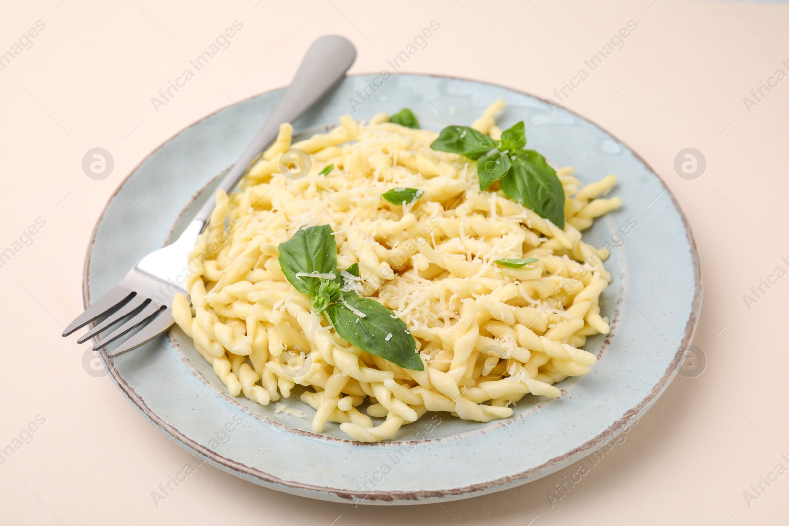Photo of Plate of delicious trofie pasta with cheese, basil leaves and fork on beige background