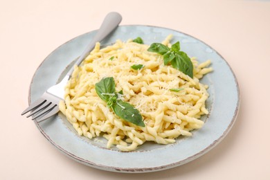 Plate of delicious trofie pasta with cheese, basil leaves and fork on beige background
