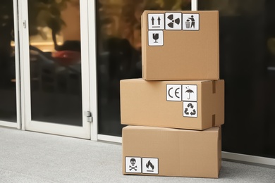 Photo of Cardboard boxes with different packaging symbols on floor near entrance, space for text. Parcel delivery