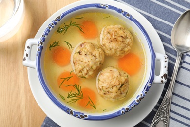 Bowl of Jewish matzoh balls soup on wooden table, top view