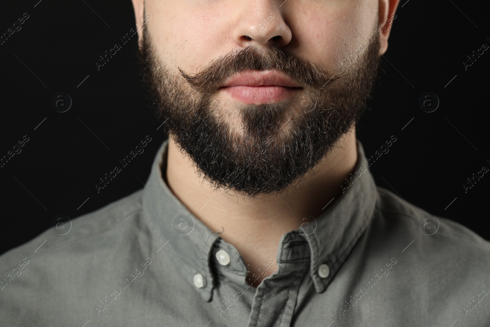 Photo of Handsome young man with mustache on black background, closeup