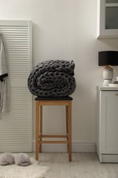 Photo of Wooden stool with rolled chunky knit blanket in room
