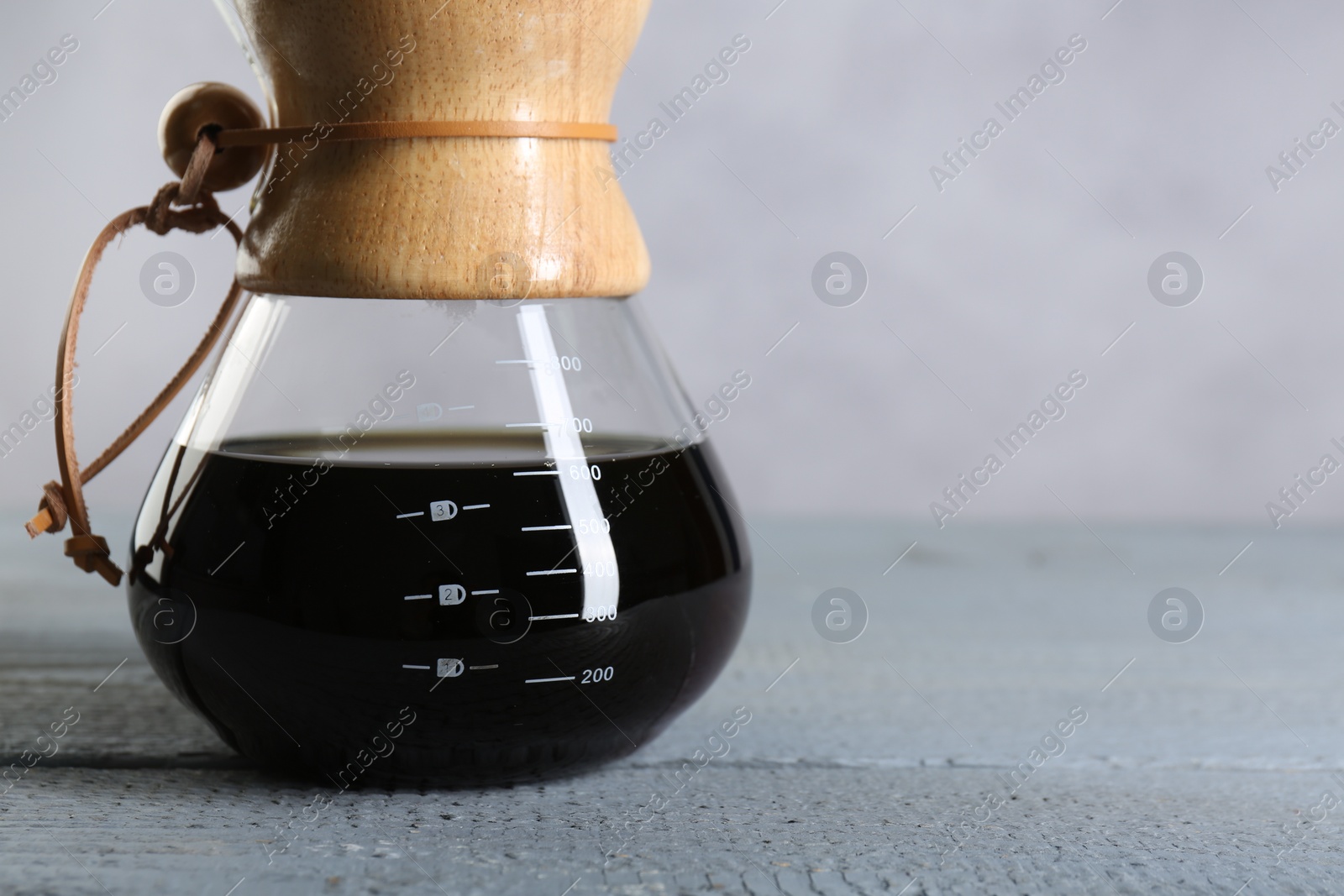 Photo of Glass chemex coffeemaker with tasty drip coffee on grey wooden table, closeup. Space for text