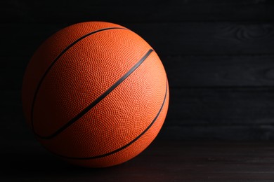 Photo of Basketball ball on wooden table against dark background, space for text