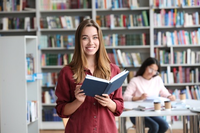 Young pretty woman with book in library