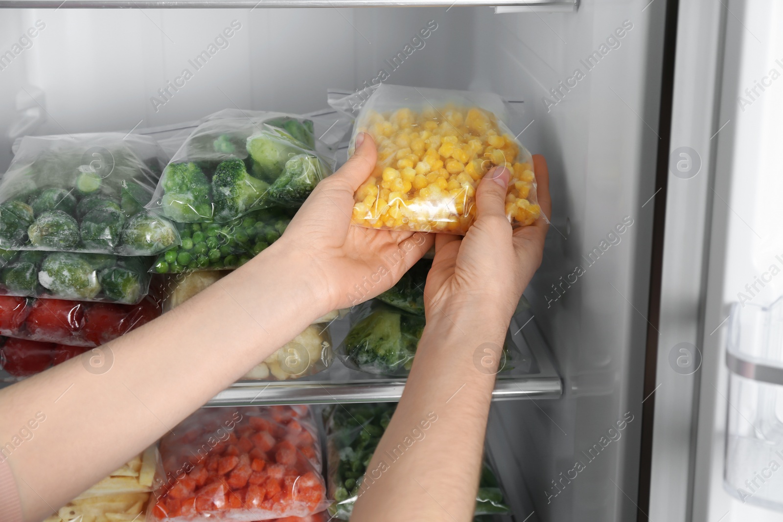 Photo of Woman taking plastic bag with frozen corn from refrigerator, closeup