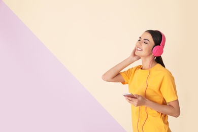 Attractive woman with mobile phone enjoying music in headphones on color background. Space for text