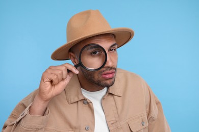 Man looking through magnifier glass on light blue background