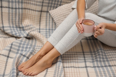 Photo of Woman with cup of coffee sitting on checkered plaid, closeup