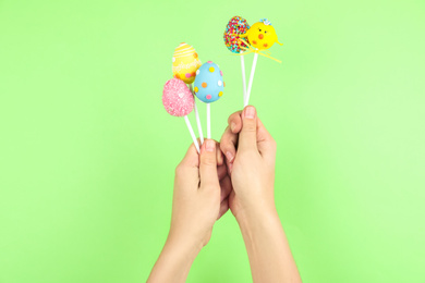 Photo of Woman with delicious cake pops on light green background, closeup. Easter holiday