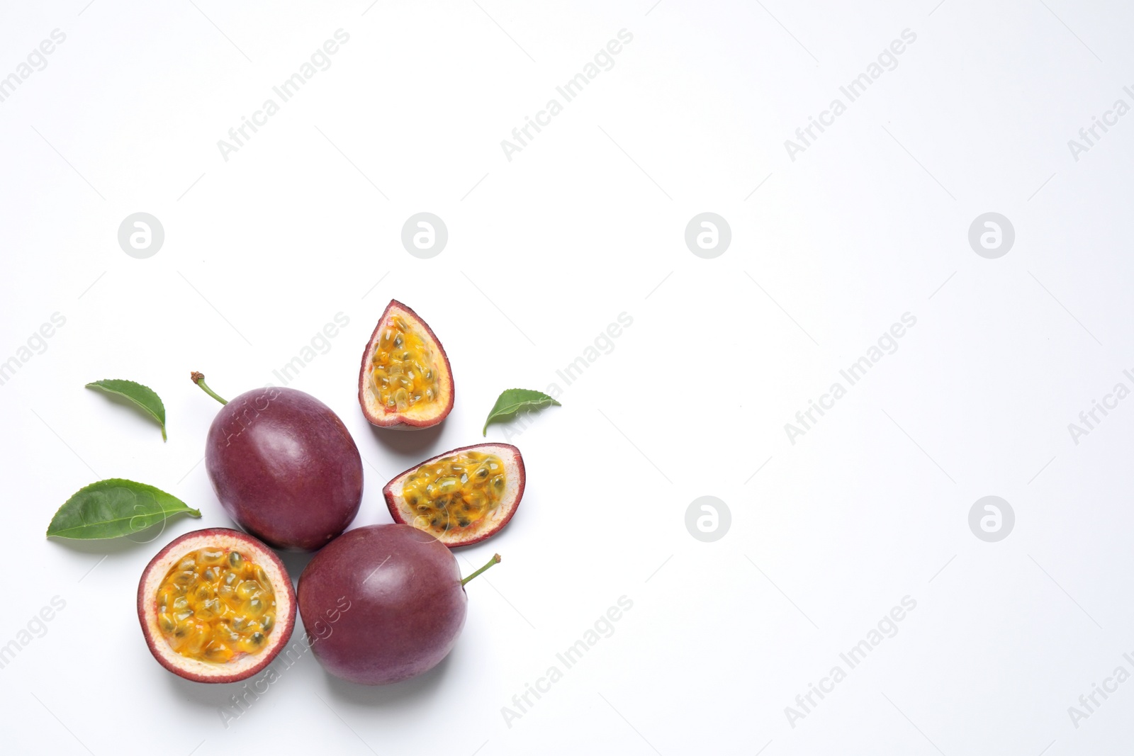 Photo of Fresh ripe passion fruits (maracuyas) with leaves on white background, flat lay. Space for text