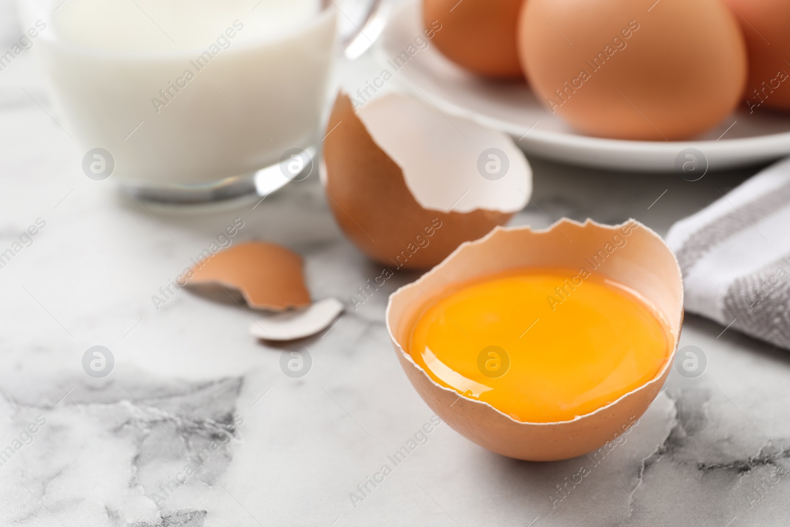 Photo of Cracked eggshell with raw yolk on white marble table, closeup. Space for text