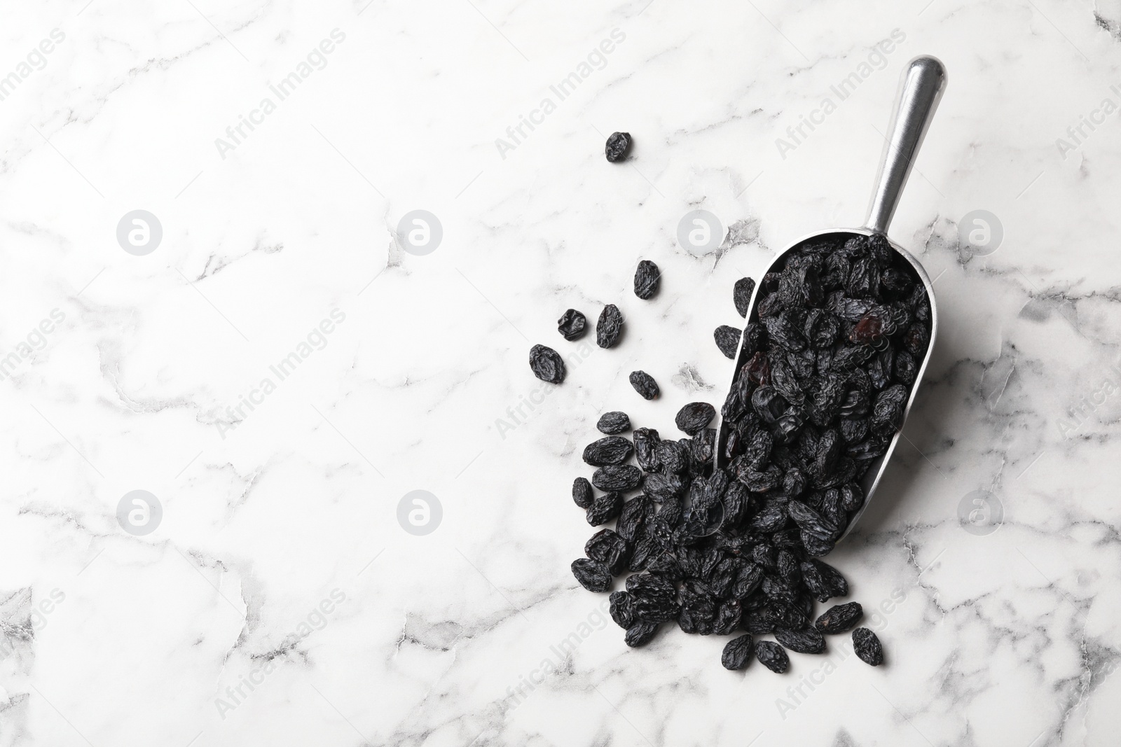 Photo of Scoop with raisins and space for text on marble background, top view. Dried fruit as healthy snack