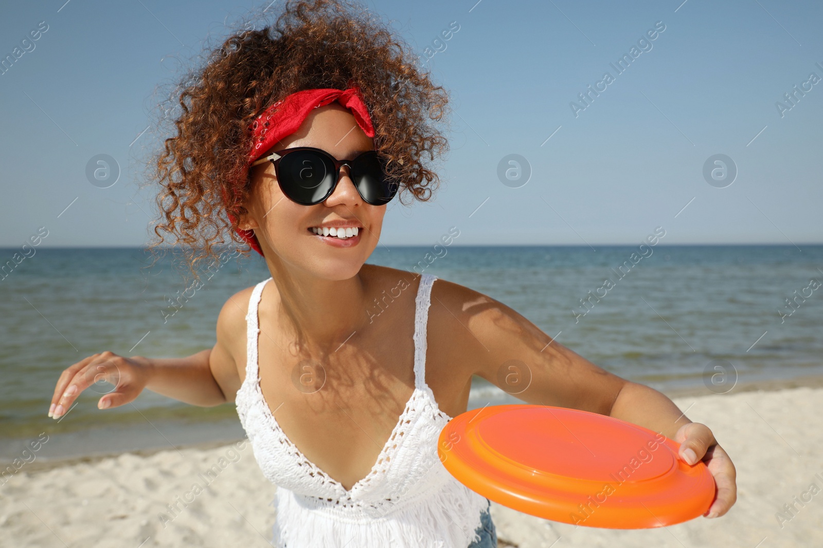 Photo of Happy African American woman throwing flying disk at beach on sunny day