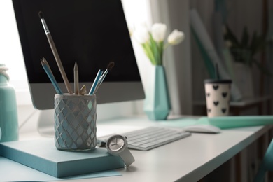 Stylish workplace with modern computer on desk. Focus on pencil holder and watch