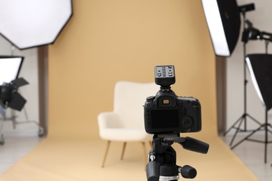 Camera on tripod, armchair and professional lighting equipment in modern photo studio, space for text