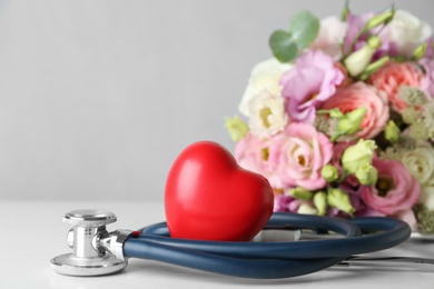 Photo of Red heart, stethoscope and bouquet on white table. World health day