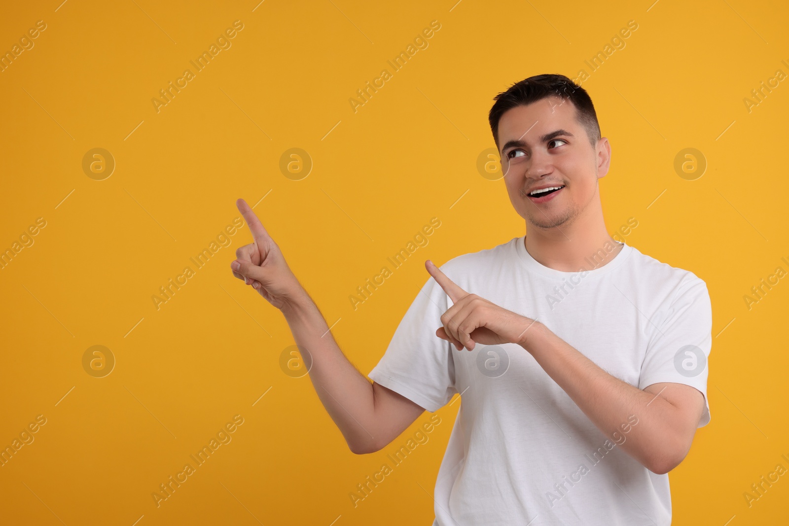 Photo of Special promotion. Happy man pointing at something on orange background, space for text