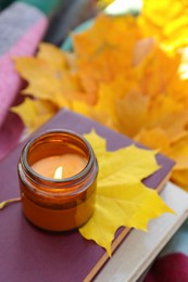 Burning candle, books and dry leaves, above view. Autumn atmosphere