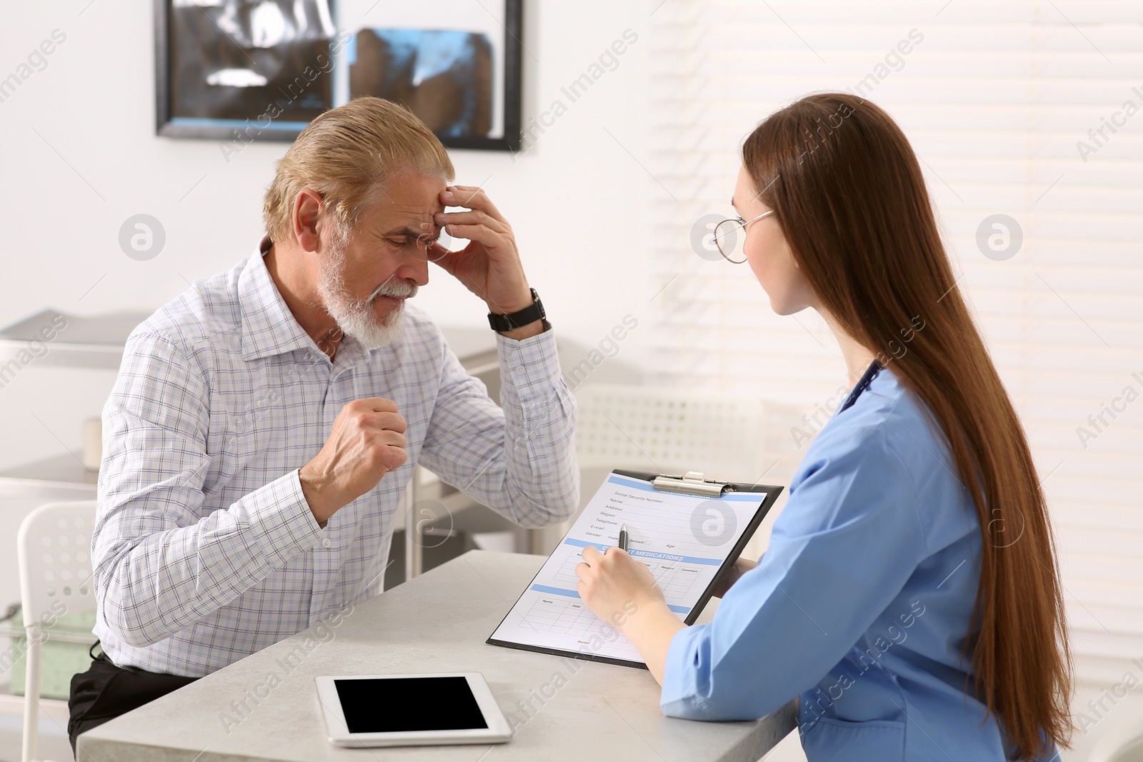 Photo of Doctor showing medical card to patient at table in clinic