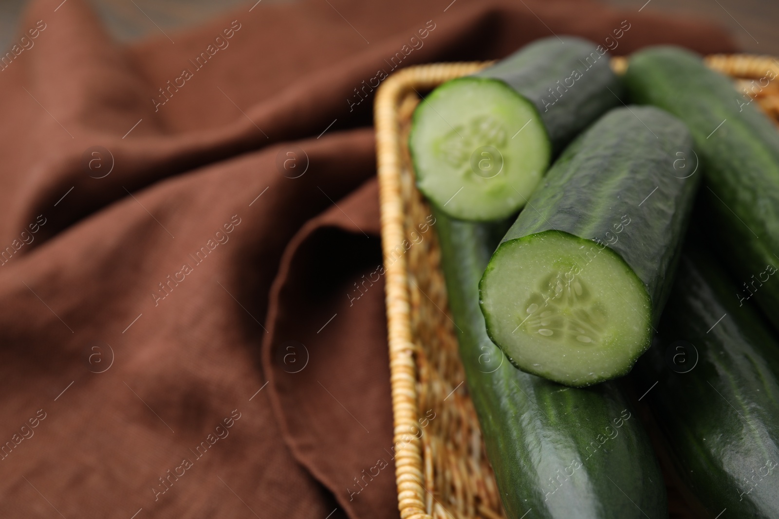 Photo of Fresh cucumbers in wicker basket on table, closeup. Space for text