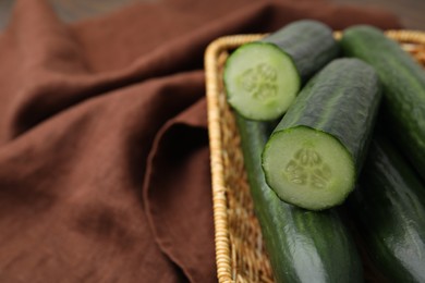 Fresh cucumbers in wicker basket on table, closeup. Space for text