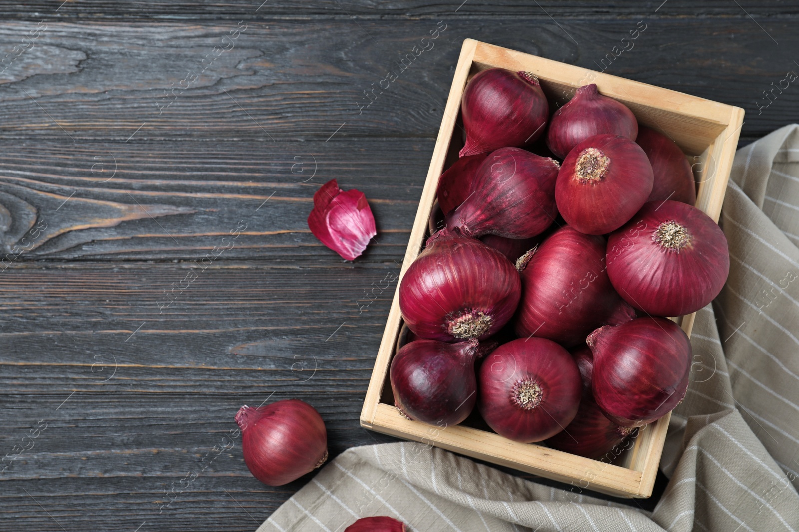 Photo of Crate with whole red onion bulbs and space for text on dark wooden background, flat lay