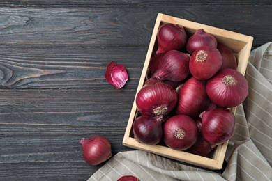 Crate with whole red onion bulbs and space for text on dark wooden background, flat lay