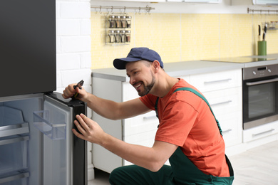 Male technician with pliers repairing refrigerator indoors