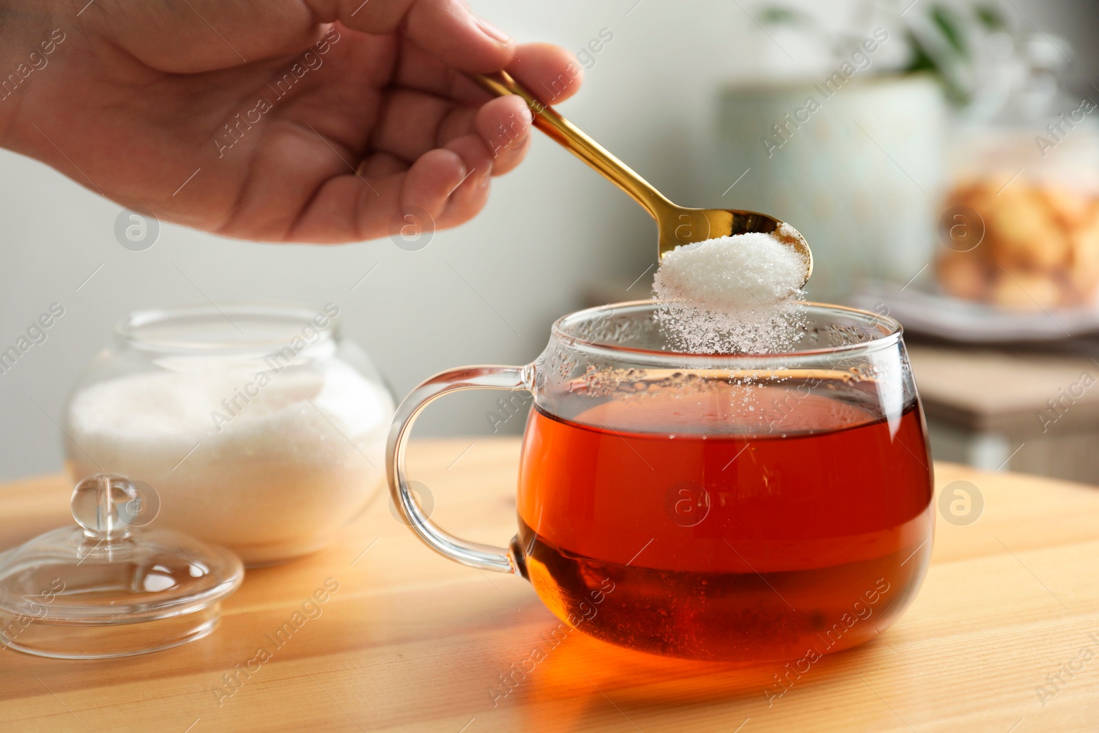 Photo of Woman adding sugar into aromatic tea at wooden table indoors, closeup