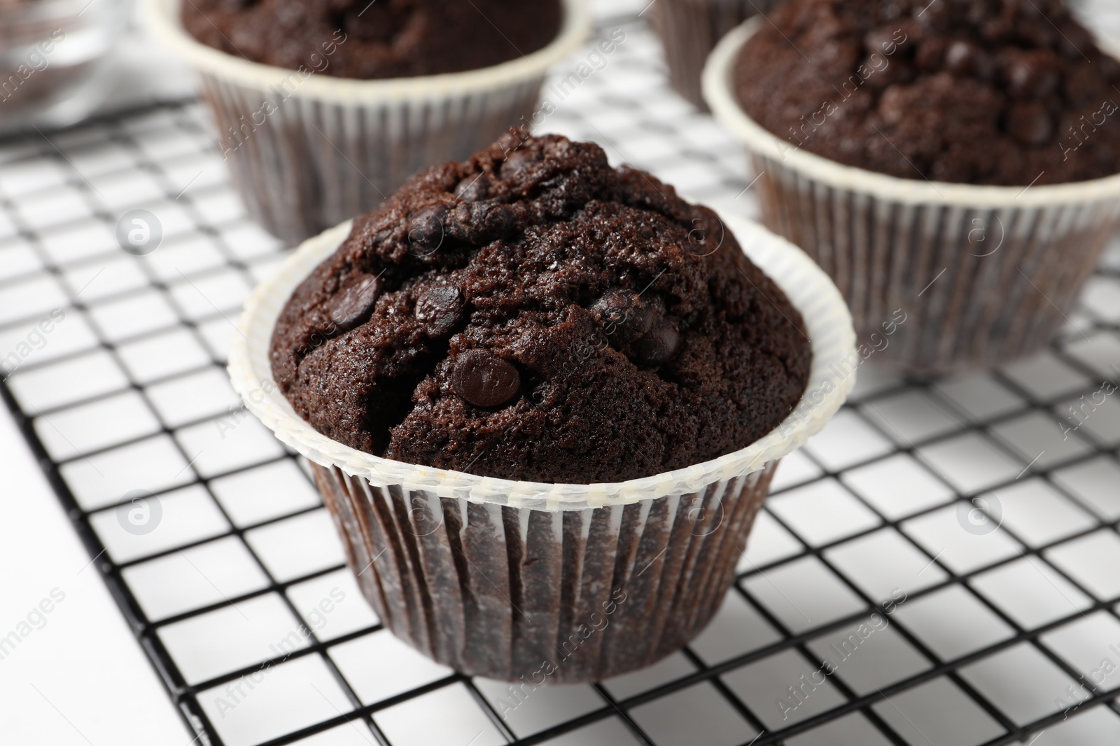 Photo of Tasty chocolate muffins and cooling rack on white table, closeup