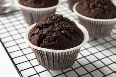 Photo of Tasty chocolate muffins and cooling rack on white table, closeup