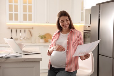 Pregnant woman working in kitchen at home. Maternity leave