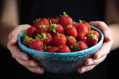 Photo of Woman holding bowl with tasty strawberries on black background, closeup