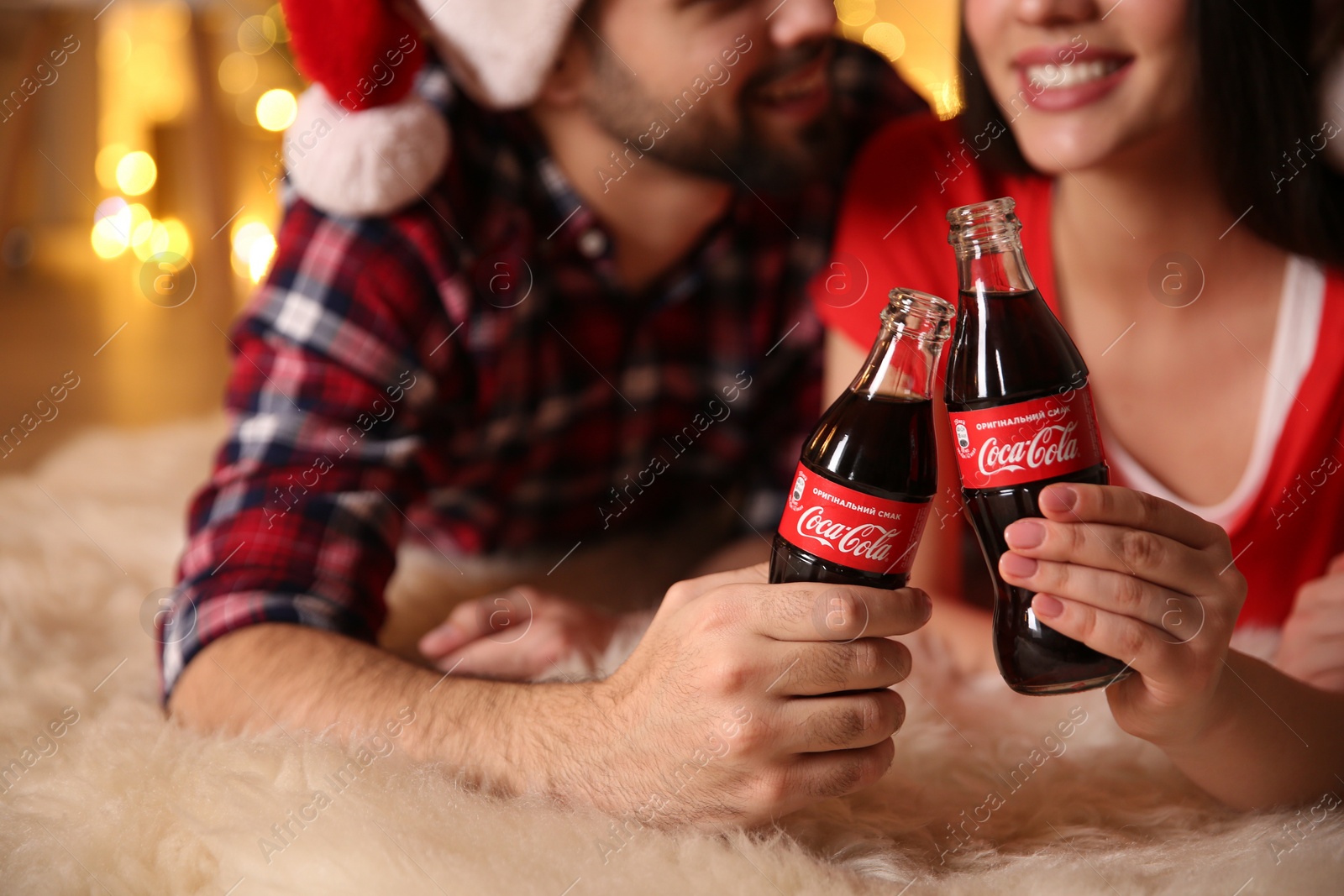 Photo of MYKOLAIV, UKRAINE - JANUARY 27, 2021: Young couple holding bottles of Coca-Cola in room with Christmas lights, closeup