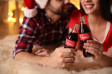 Photo of MYKOLAIV, UKRAINE - JANUARY 27, 2021: Young couple holding bottles of Coca-Cola in room with Christmas lights, closeup