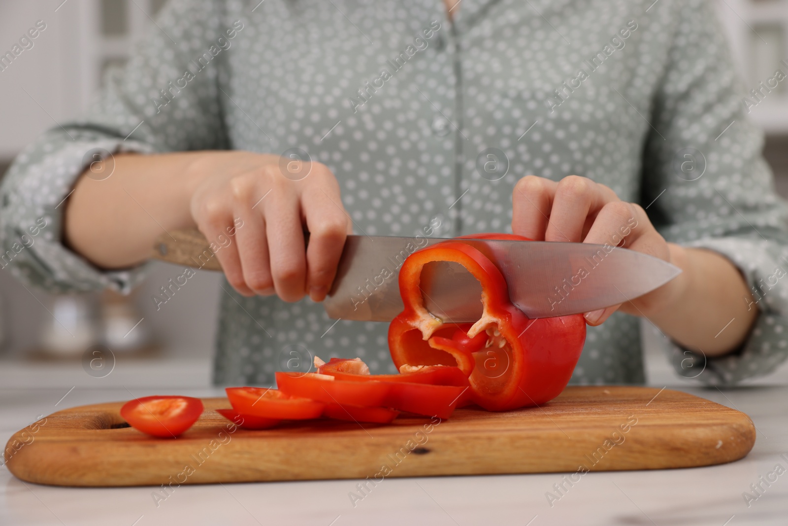 Photo of Cooking process. Woman cutting bell pepper at white countertop in kitchen, closeup